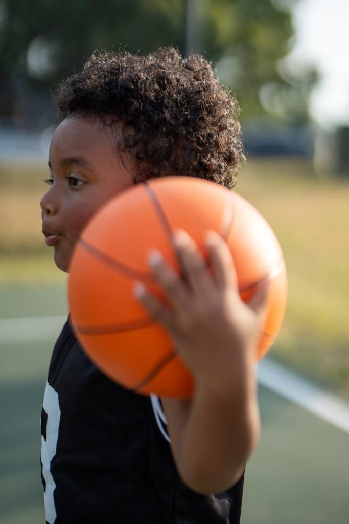 A young boy holding a basketball on an outdoor court, enjoying a sunny day.